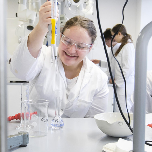 Tri nasmejane osebe v laboratoriju v laboratorijskih haljah in delu s spojinami.